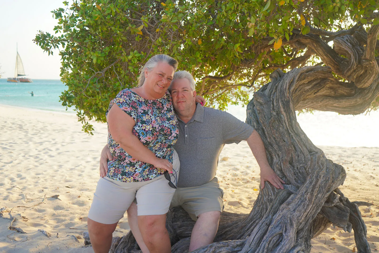 Couple leaning on a twisted tree on a white beach in Aruba