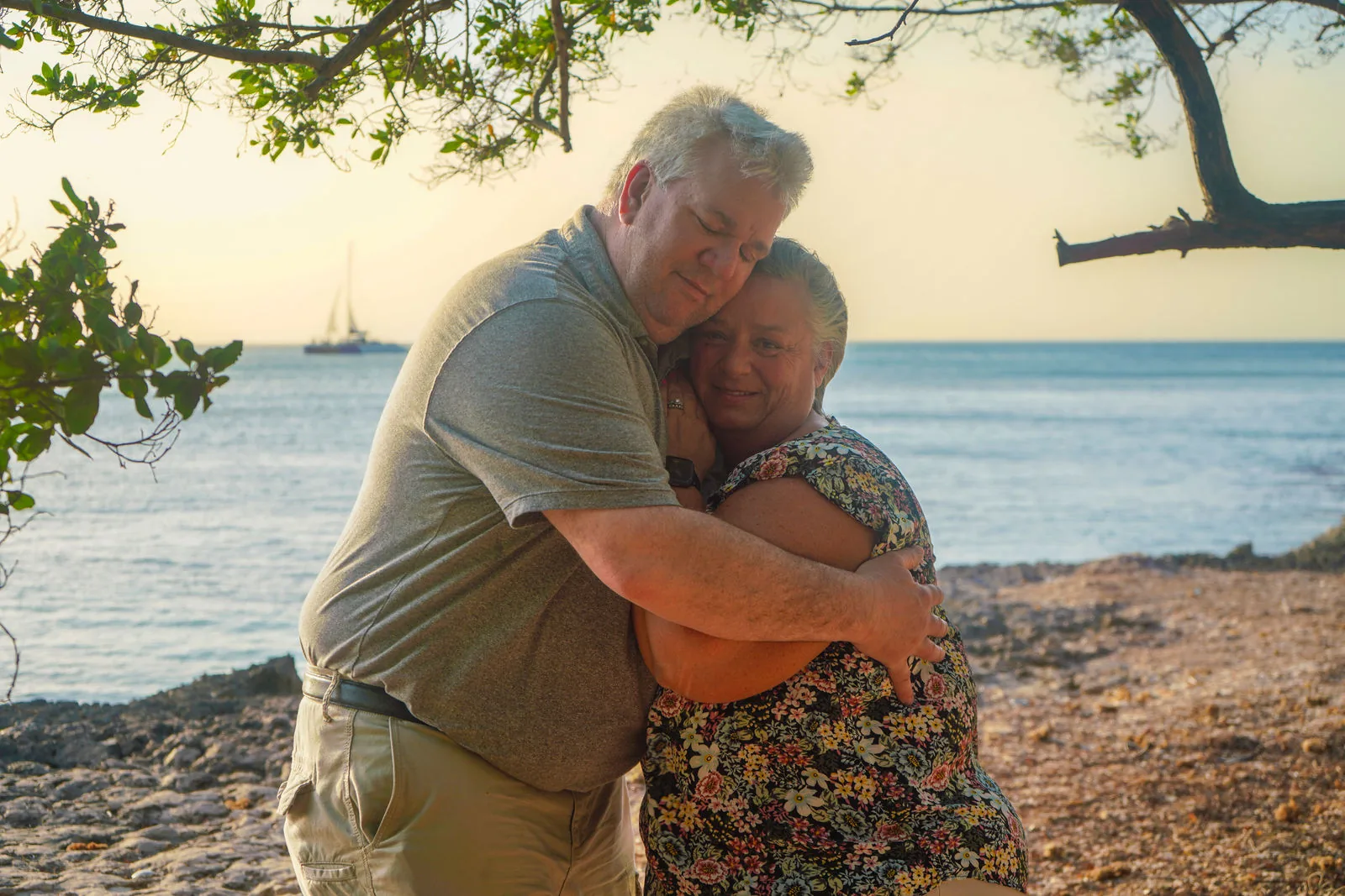 Couple hugging by the sea with sailboats behind them in Aruba