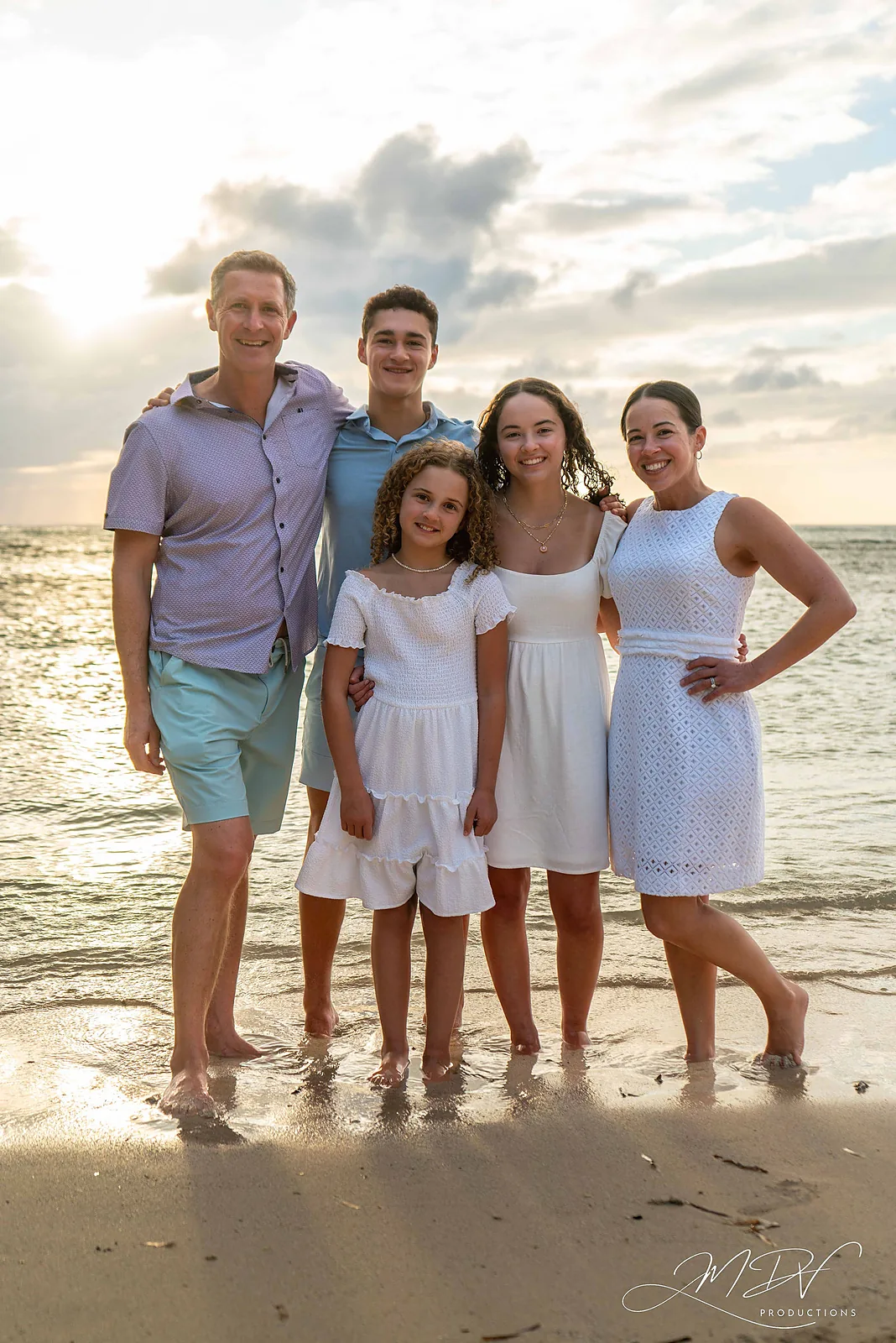 Family of five standing barefoot at the water's edge at sunset in Aruba
