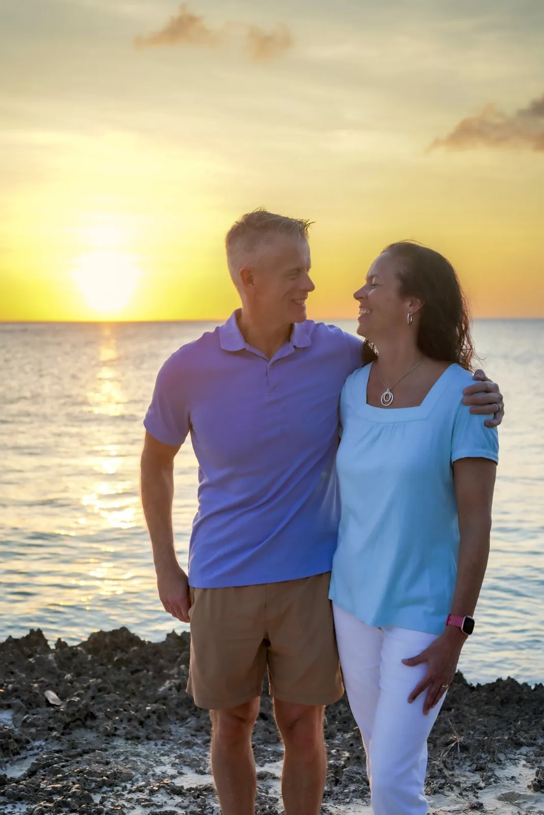 Couple smiling at each other on the rocks at sunset in Aruba