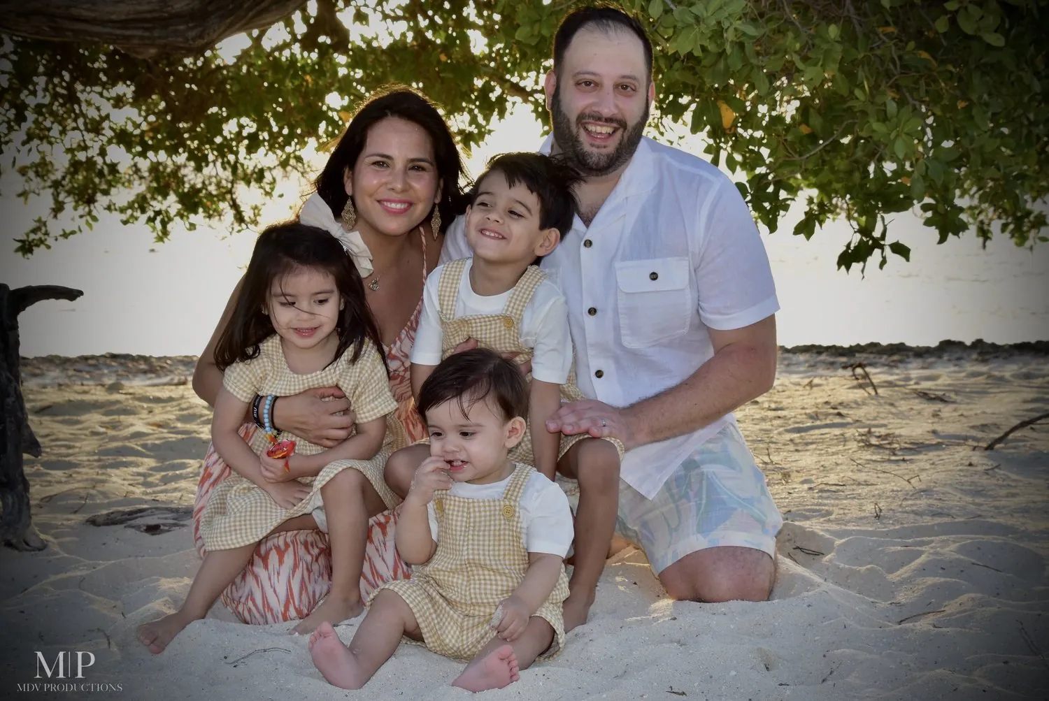 Parents with three young children on the sand under a tree in Aruba