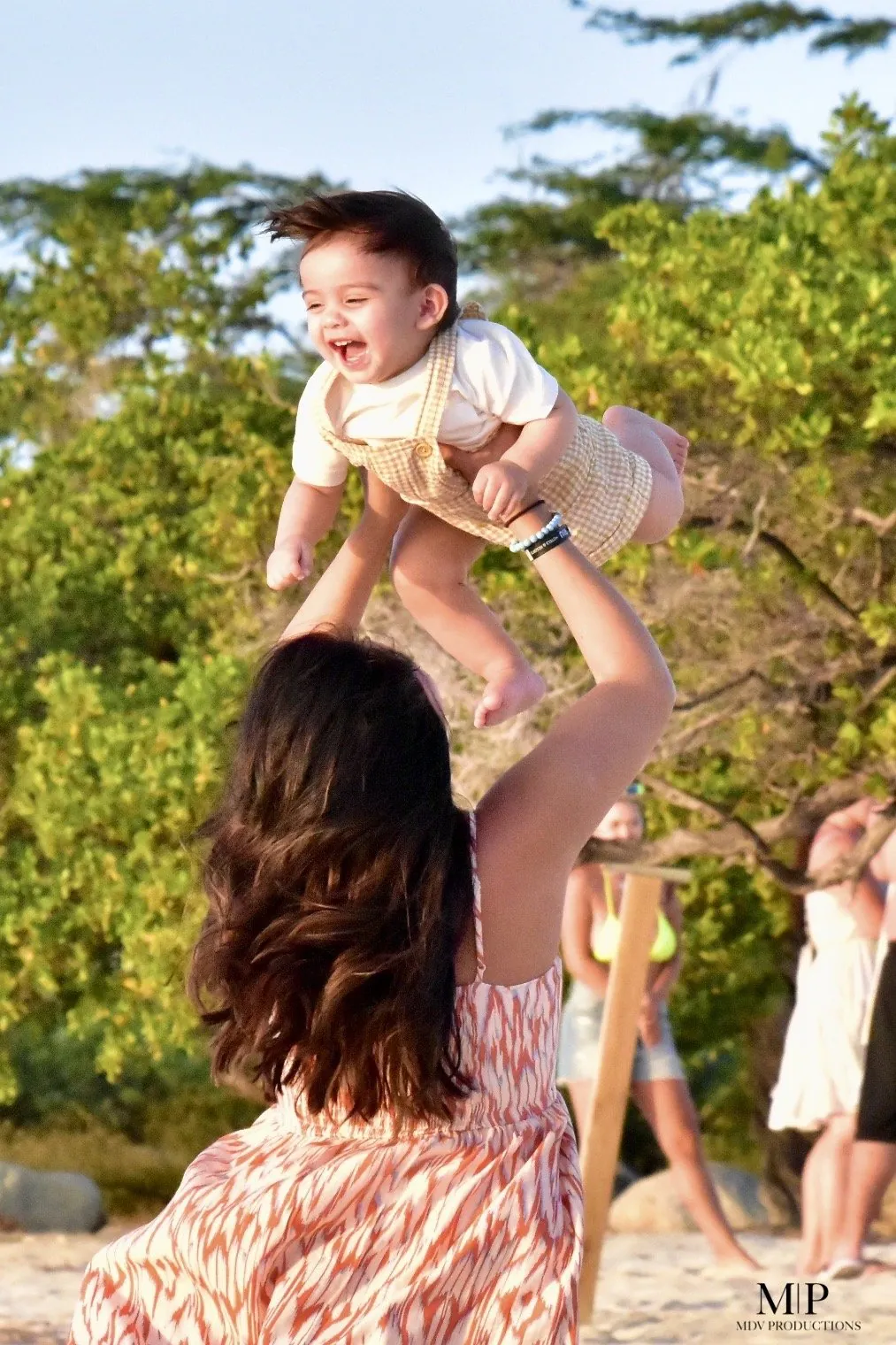 Mother lifting her laughing baby into the air on an Aruba beach