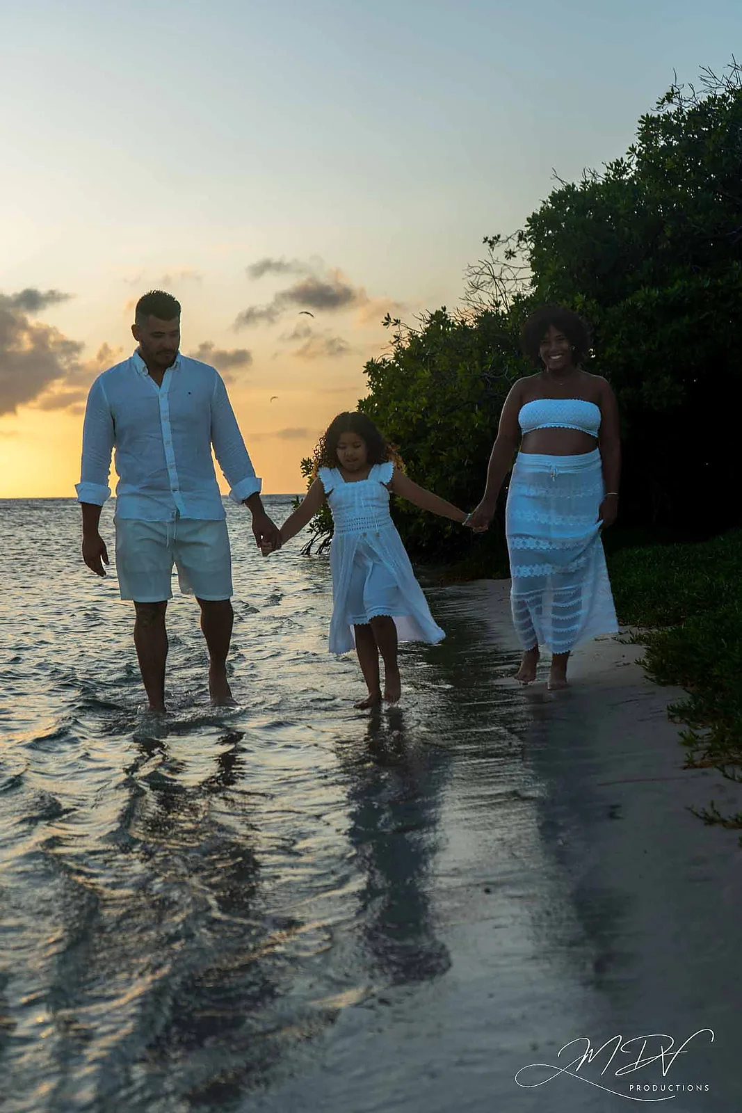 Expecting parents walking hand in hand with their daughter through the water in Aruba