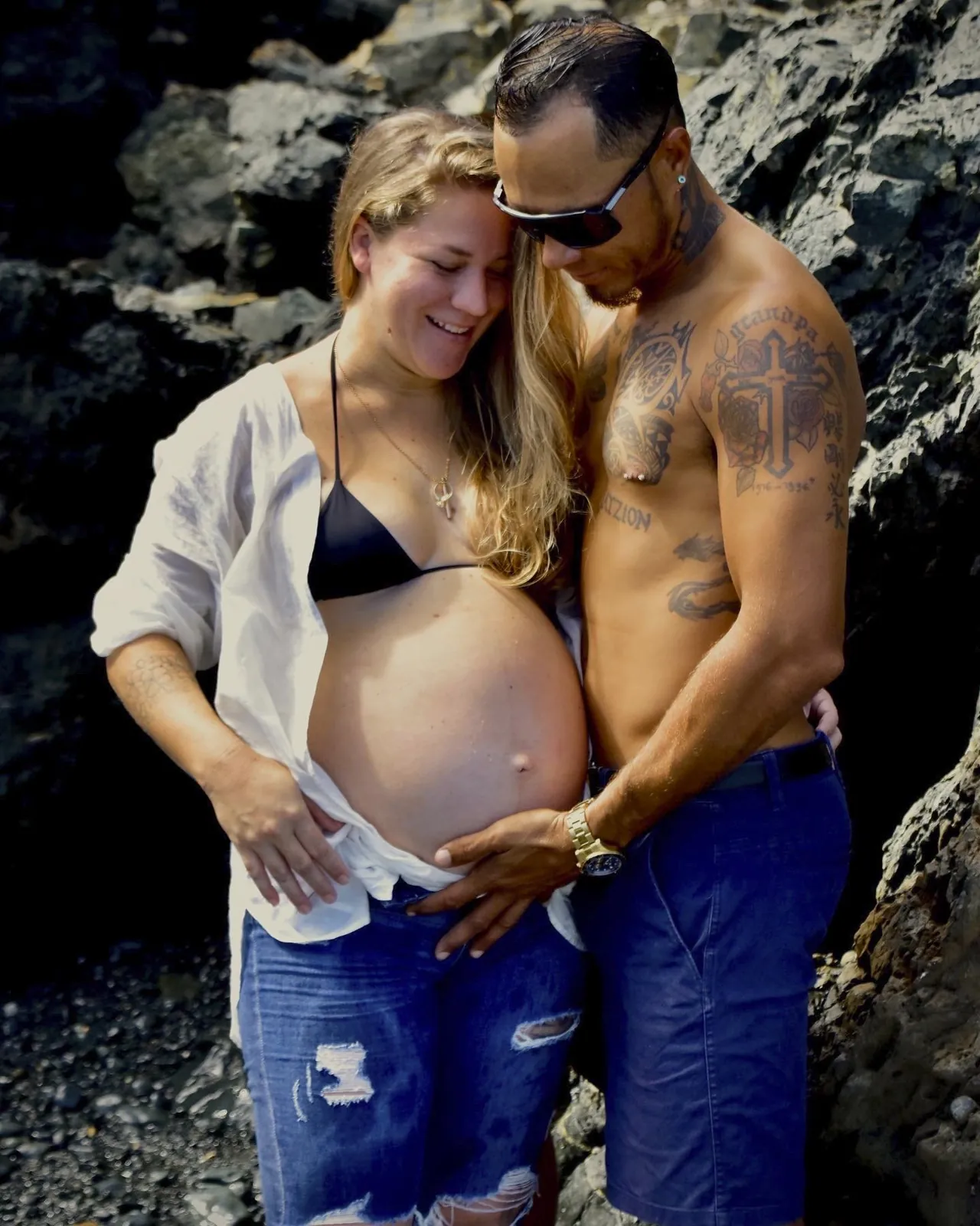 Expecting couple with their hands on the belly against dark rocks in Aruba
