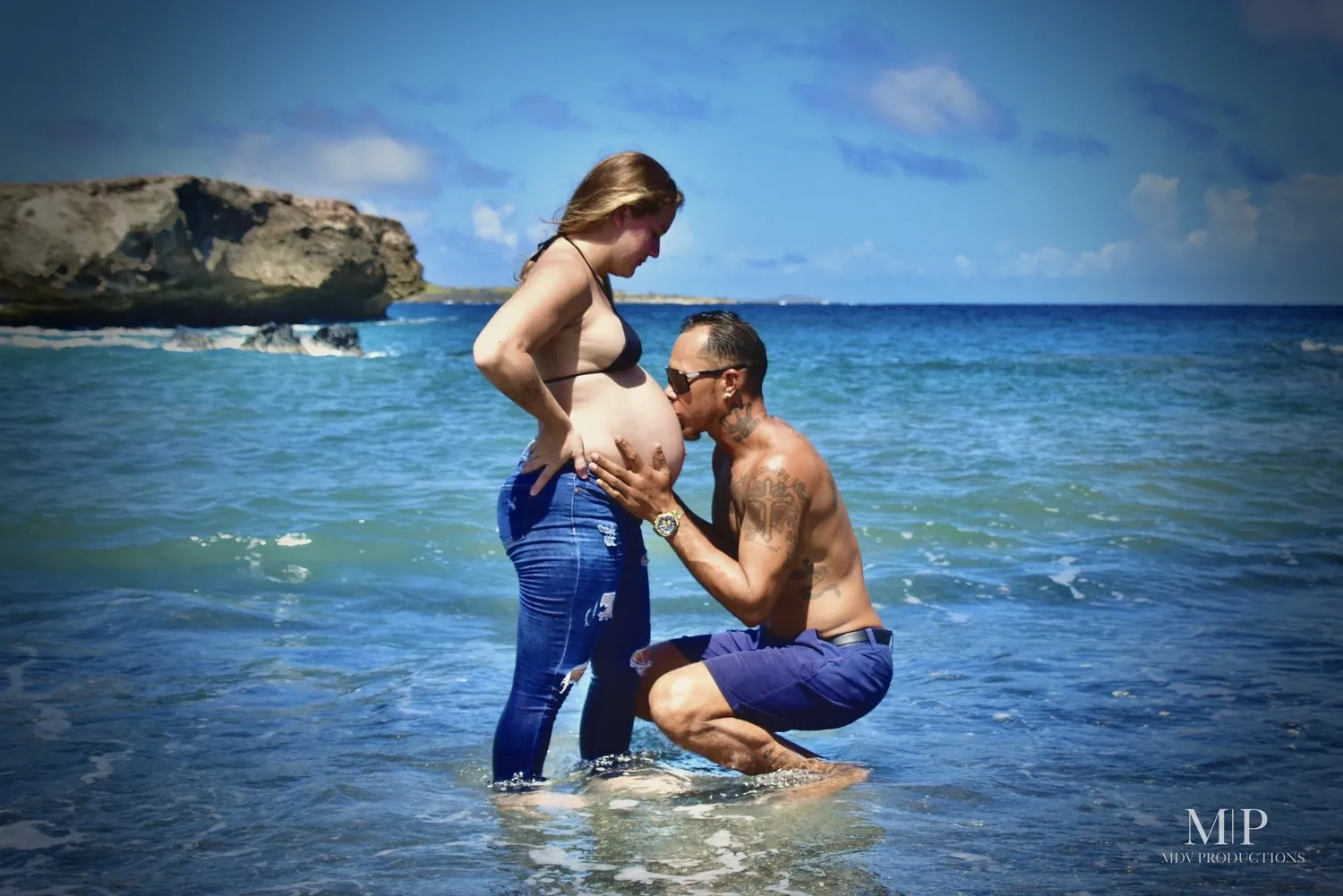 Partner kissing the belly while the couple stands in the sea in Aruba