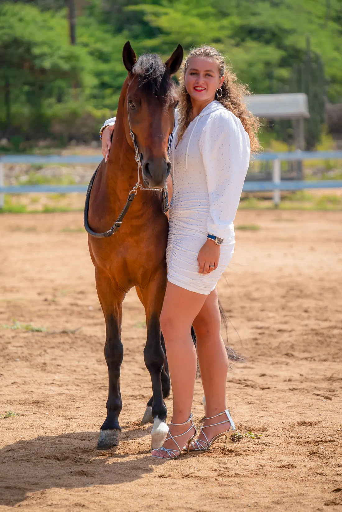 Woman in a white dress standing with Prometido in the riding arena on Aruba