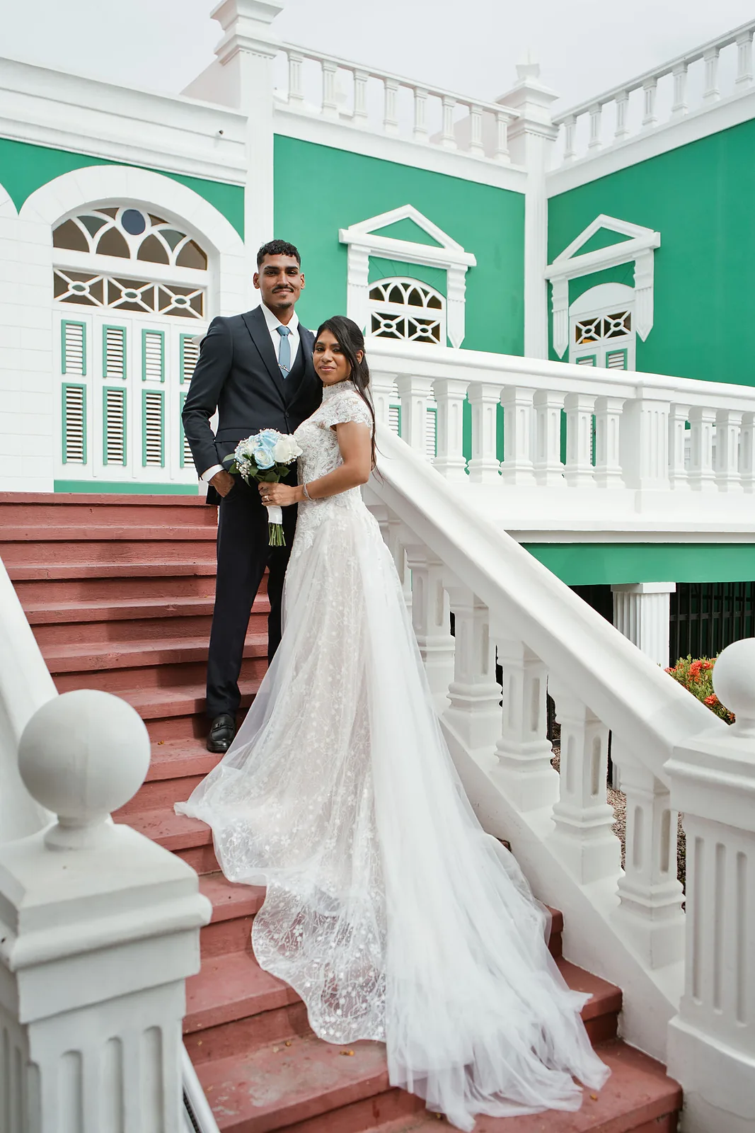 Bride and groom on the red stairs of a green colonial building in Aruba