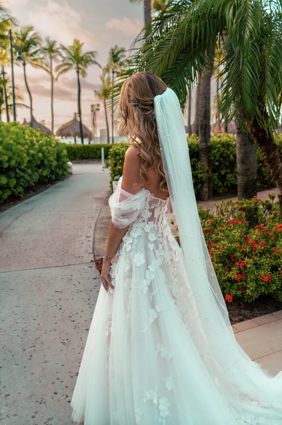 Bride with a long veil walking along a path with palm trees in Aruba